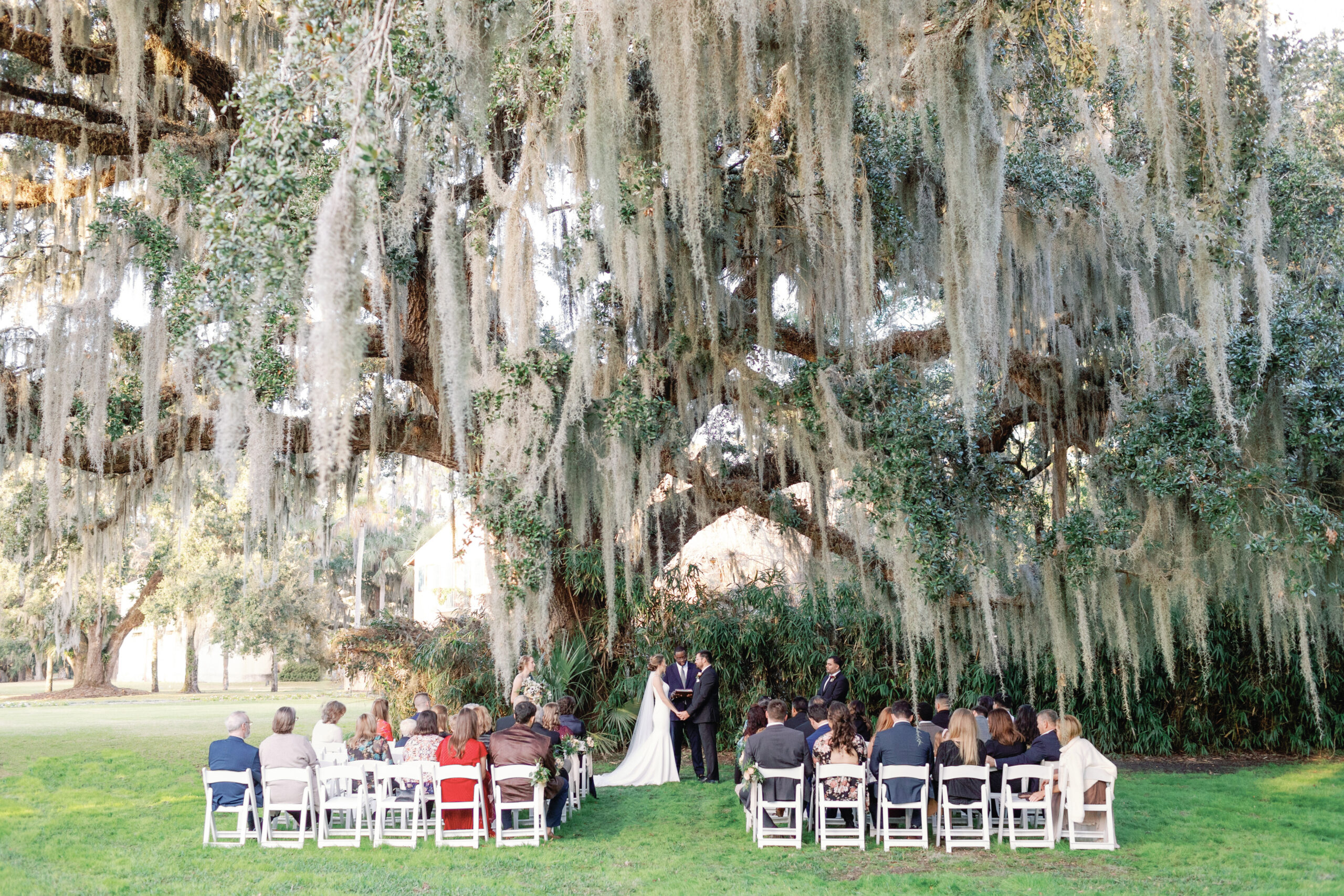 Bride and groom hold hands under large oak at Jekyll Island Club