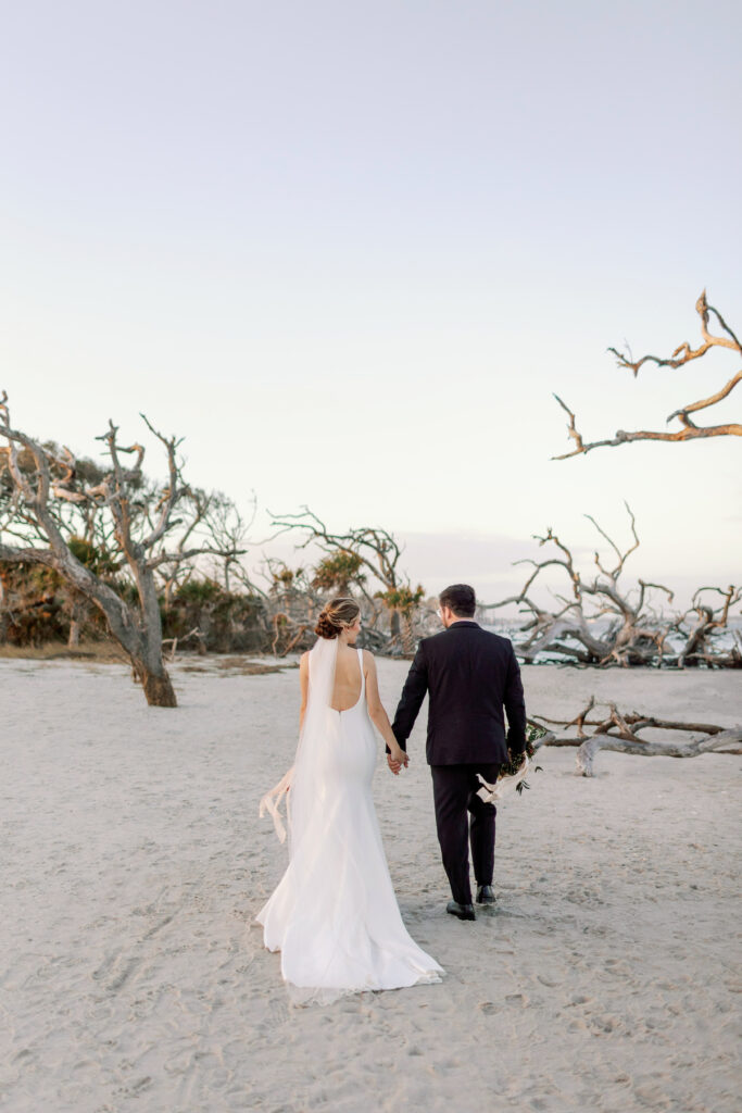 A bride and groom stand on driftwood beach.