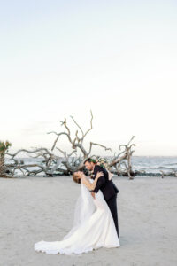A groom dips his bride on driftwood beach.