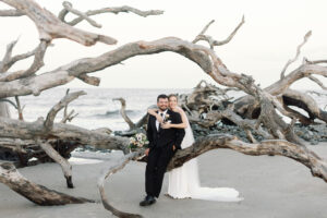 A bride hugs her groom on a piece of driftwood.