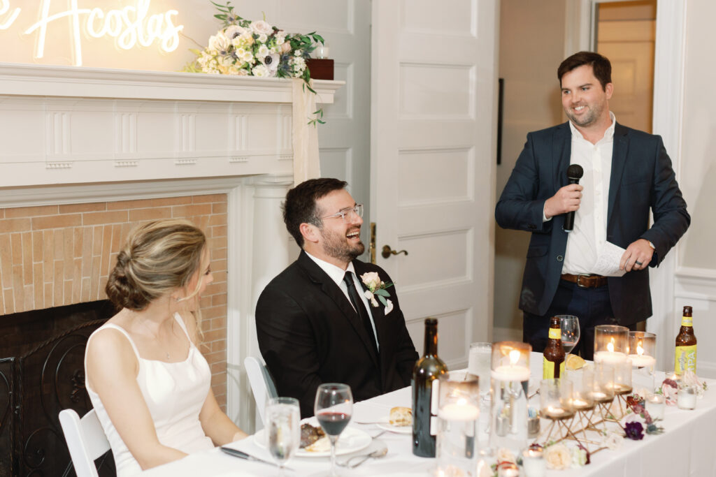 A groom seated at a table laughing.