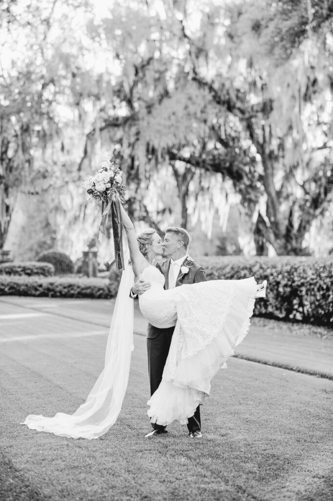 A groom holds his bride in his arms while he kisses her. 
