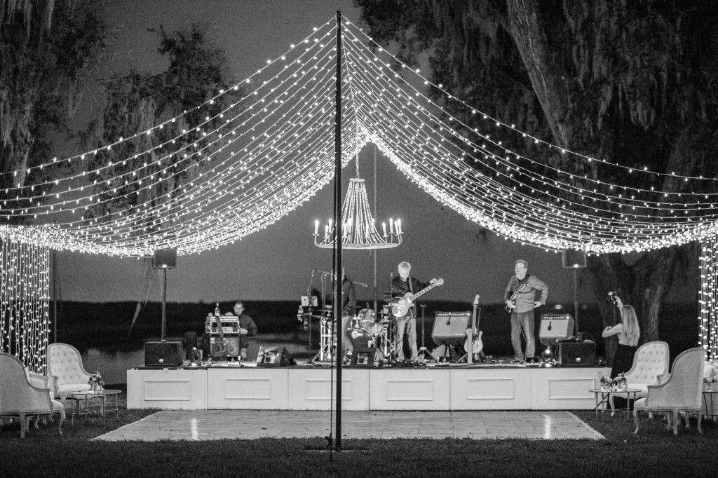 A band under a tent of lights tune their instruments. 