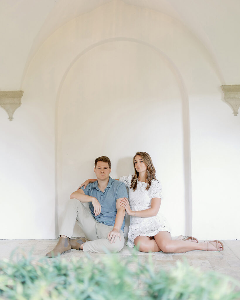 A couple sits against a white wall at Sea Island. 